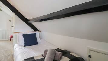 A bedroom with a sloped ceiling, a bed with a checkered blanket, a pillow, and a rolled towel.