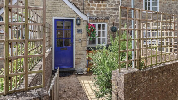 A stone house with a blue door, a small garden, and a wooden fence. - Old Ropemakers Cottage (Bridport)