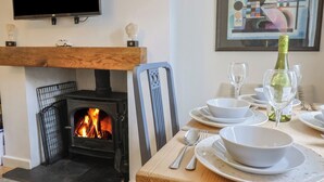 A dining area with a fireplace, a table set for two, and a bottle of wine. - Old Ropemakers Cottage (Bridport)