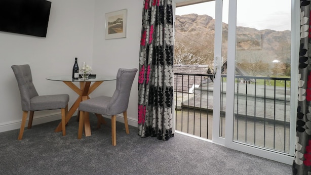 A room with a glass table, two grey chairs, a bottle of wine, and a framed picture on the wall. - Yewdale View Apartment (Coniston)