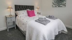 A neatly arranged bedroom with a large bed, two bedside tables with lamps, a grey and white polka dot bedspread, a single pink pillow, and a grey floral artwork on the wall. - Yewdale View Apartment (Coniston)