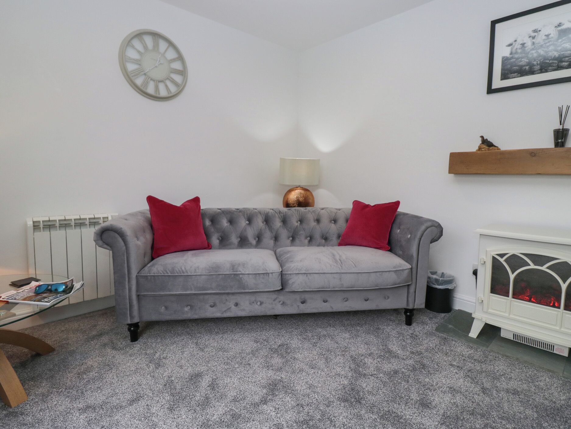 A grey sofa with red cushions, a white radiator, a clock, a lamp, and a fireplace.