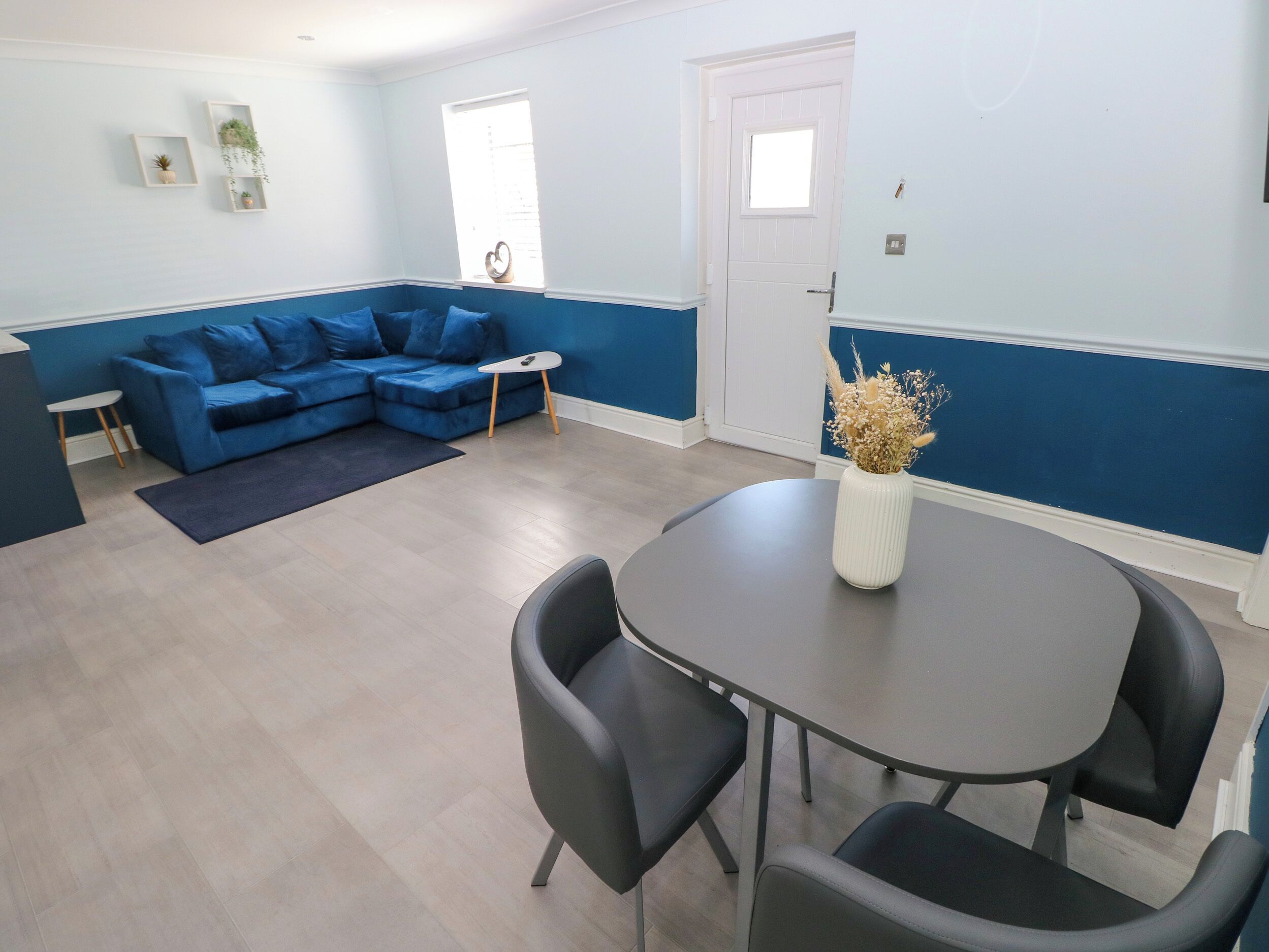 Un salon moderne avec un canapé bleu, une petite table et un vase contenant des fleurs séchées.
