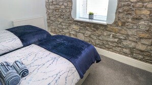 Une chambre avec deux lits, des murs en pierre, une fenêtre avec des stores et un radiateur.