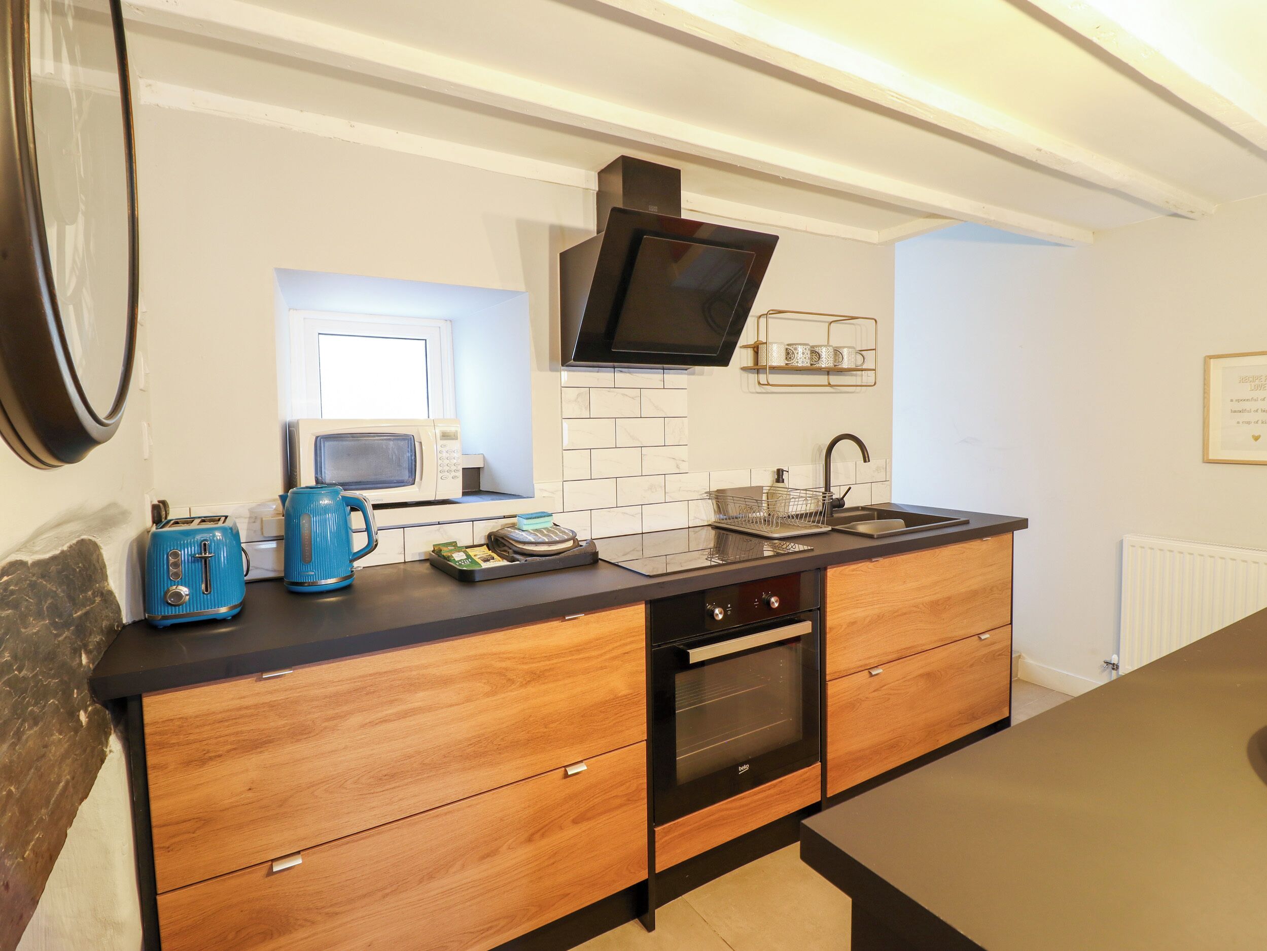 Une cuisine moderne équipée d’un four à micro-ondes, d’un grille-pain et d’une bouilloire sur le plan de travail, ainsi que d’un évier et d’un four encastré.