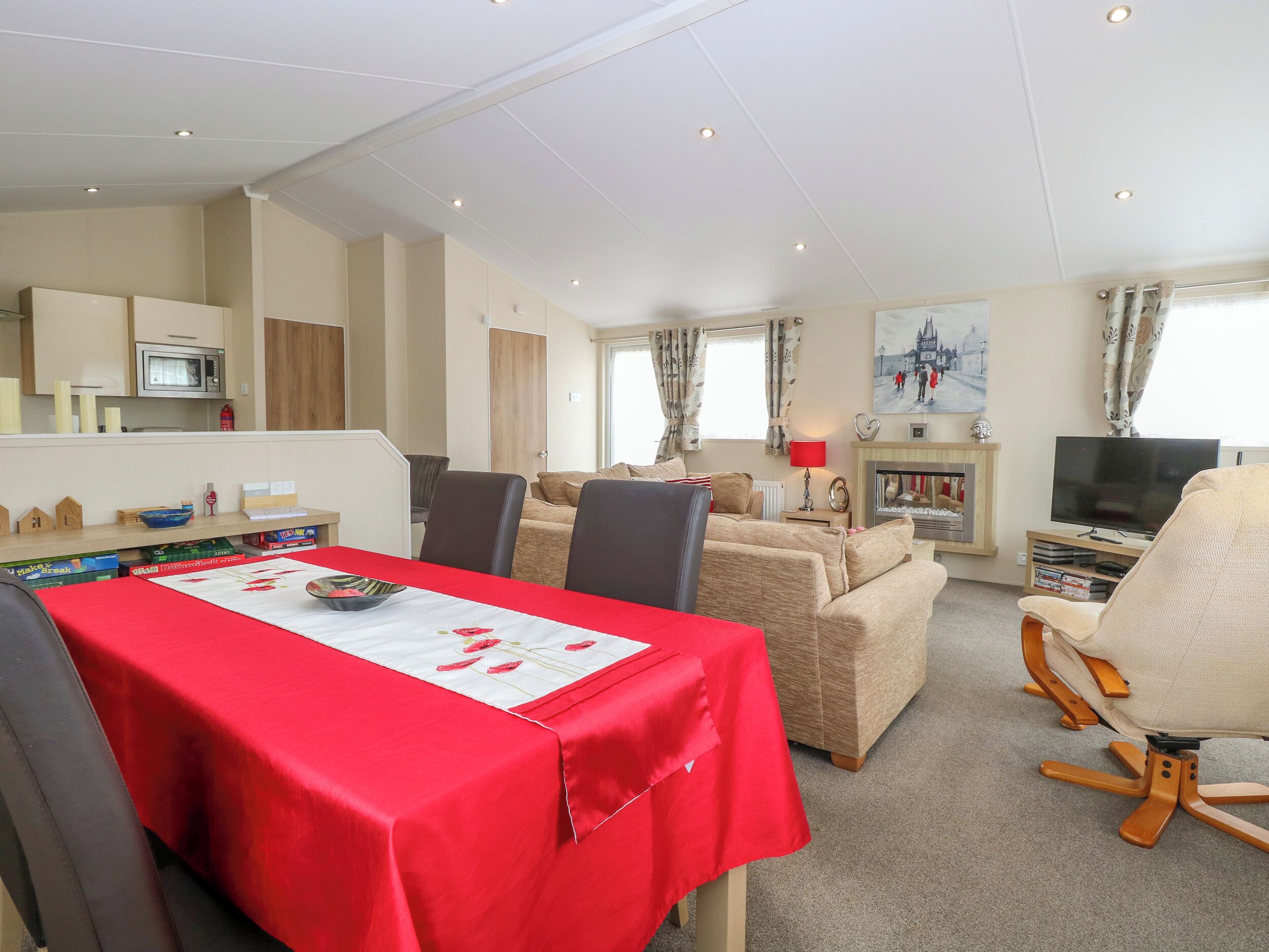Een moderne woonkamer met een rode tafel, beige banken, een televisie en een open haard.
