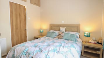 A bedroom with a bed, two bedside tables, a wooden wardrobe, and a nightstand with a lamp.