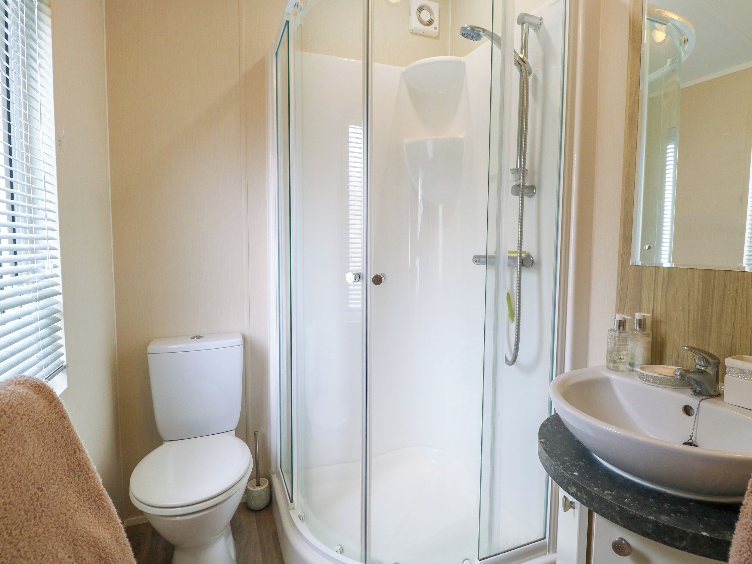 A modern bathroom with a glass-enclosed shower, a white toilet, and a sink with a marble countertop.