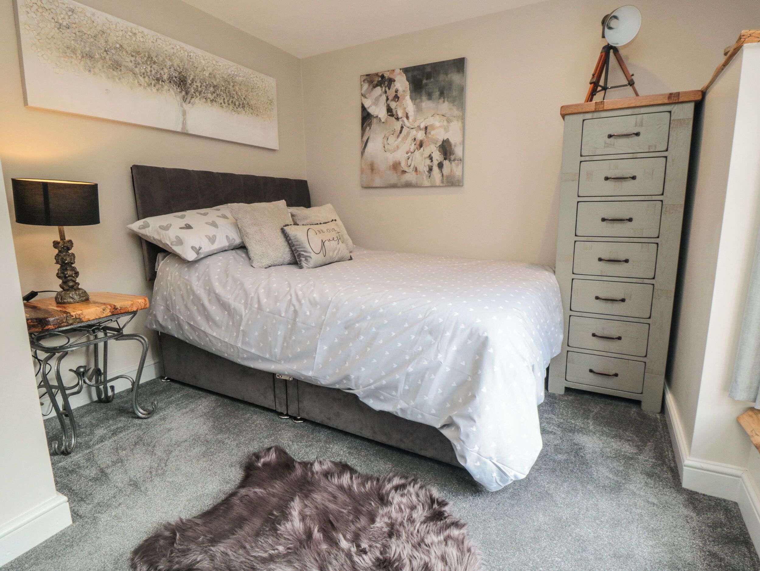 A bedroom with a bed, a desk, a lamp, a dresser, and a rug.