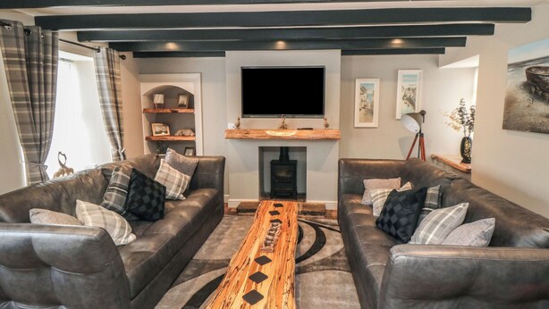 A modern living room with two leather sofas, a wooden coffee table, a flat-screen TV, and a fireplace. - 15 High Street (Scarborough)