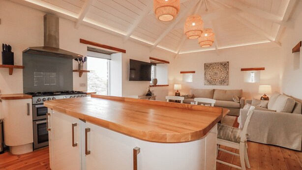 A modern kitchen with a central island, wooden flooring, and pendant lighting. - Logan Barn (Camelford)