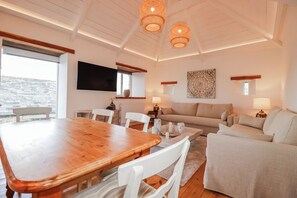 A spacious living area with a wooden dining table, white chairs, a sofa, and two lamps. - Logan Barn (Camelford)