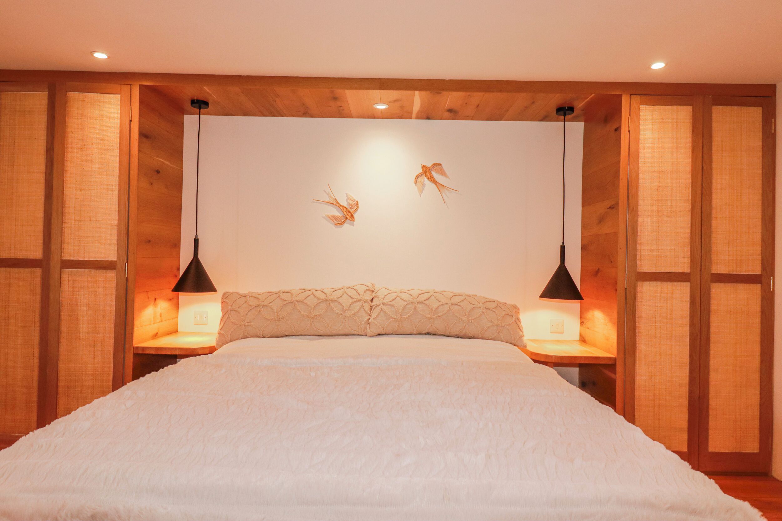 Une chambre avec un grand lit, des murs en bois et deux lampes fixées au mur.