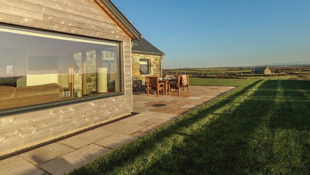 Een huis met een grote schuifpui, een stenen gevel en een terras met tuinmeubilair.