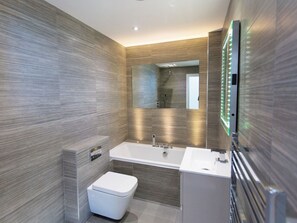 A modern bathroom with a large mirror, a bathtub, and a toilet. - 7 Atlantic Watch (St Ives)