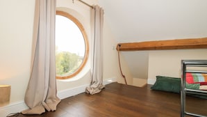 A small, cozy room with a sloped ceiling, a round window, wooden flooring, and a bunk bed. - Millstone Cottages - Breidden View (Shrewsbury)
