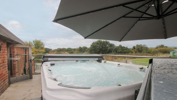A hot tub with a canopy, a brick wall, and a grassy area in the background. - Millstone Cottages - Breidden View (Shrewsbury)