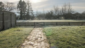 A backyard with a brick pathway, a wooden fence, and trees.