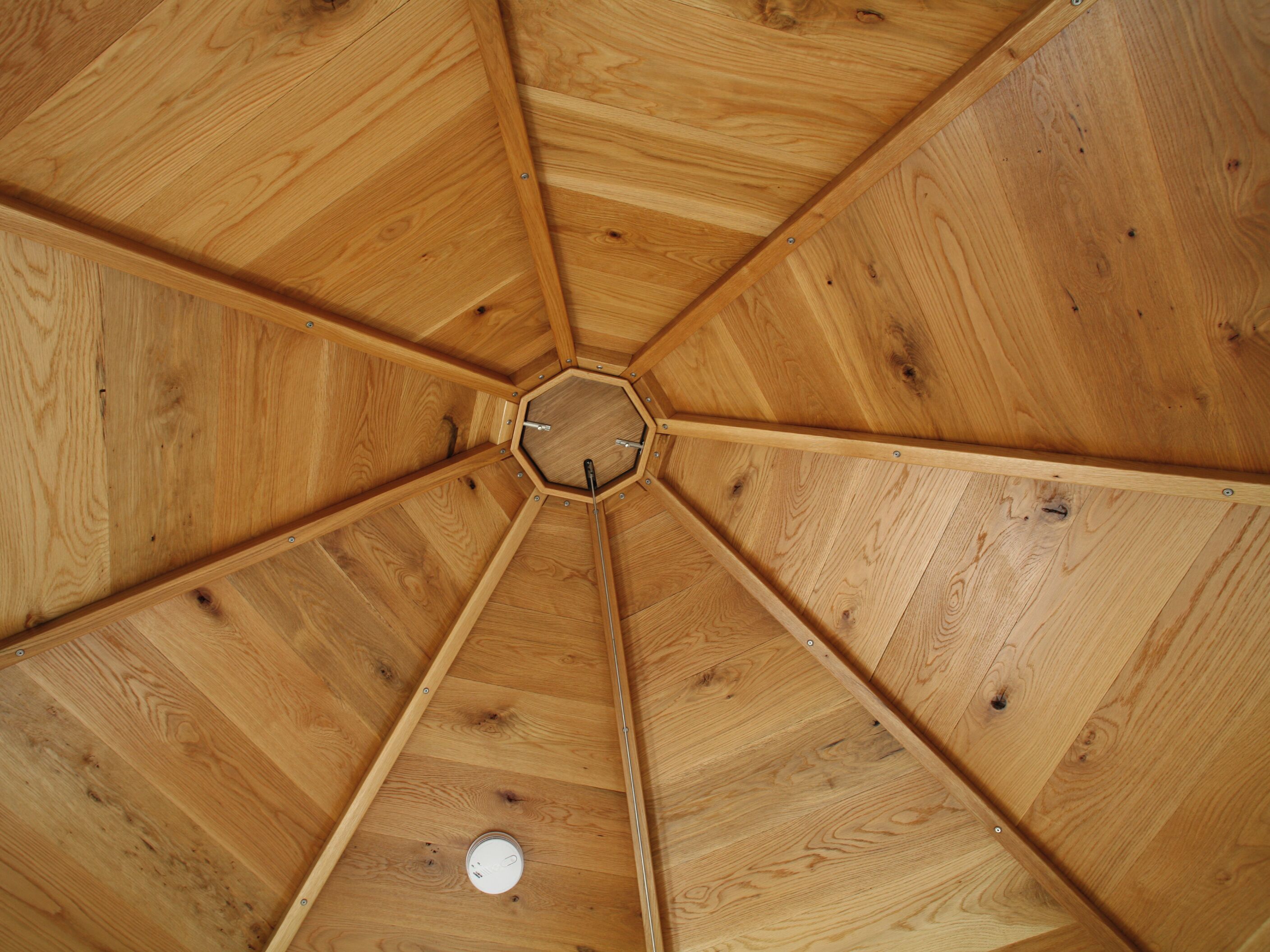 A wooden ceiling with a central hexagonal opening and a circular vent.