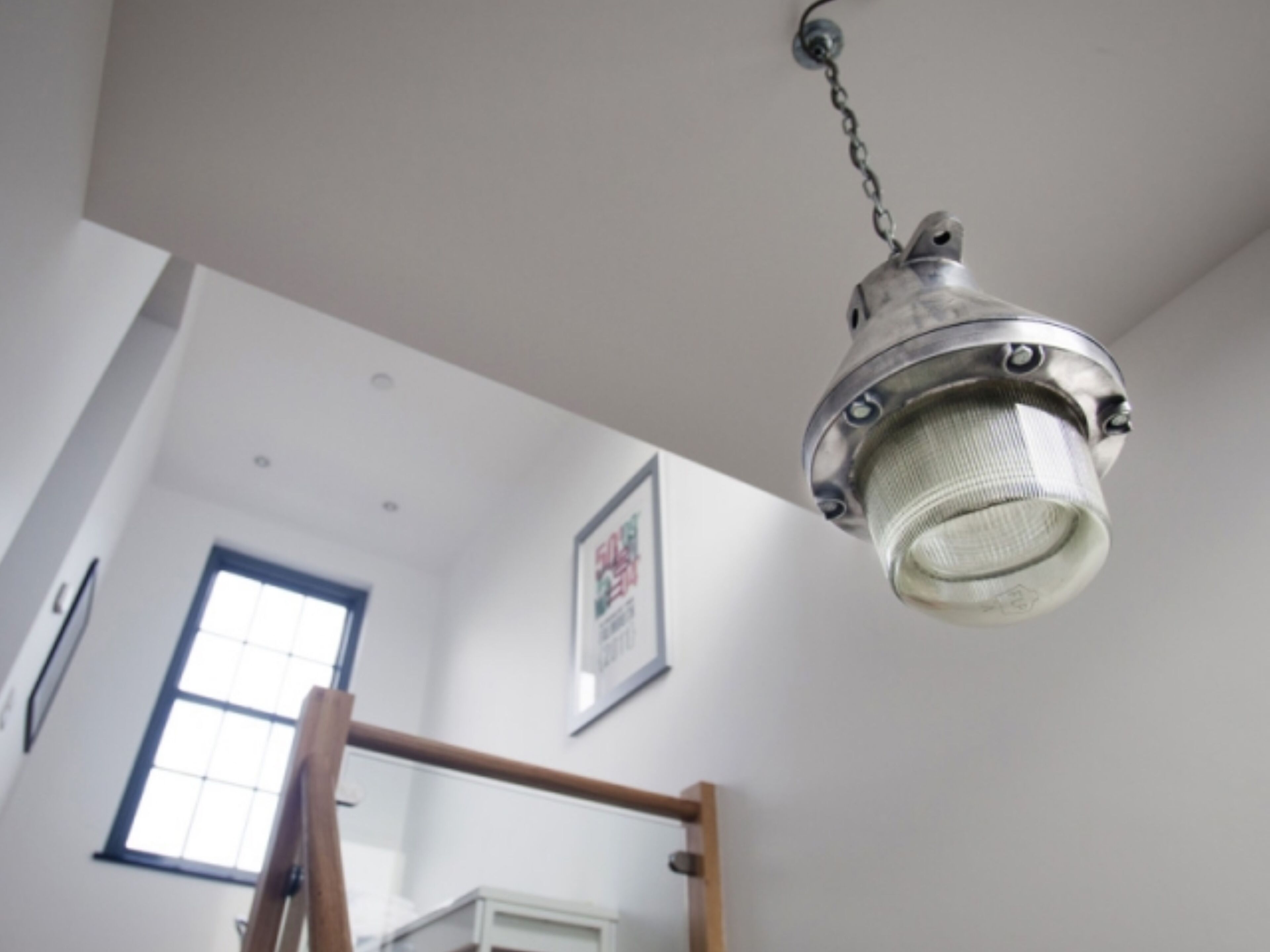 Un intérieur moderne agrémenté d’un luminaire suspendu de style industriel, d’une structure en bois et d’un tableau encadré au mur.