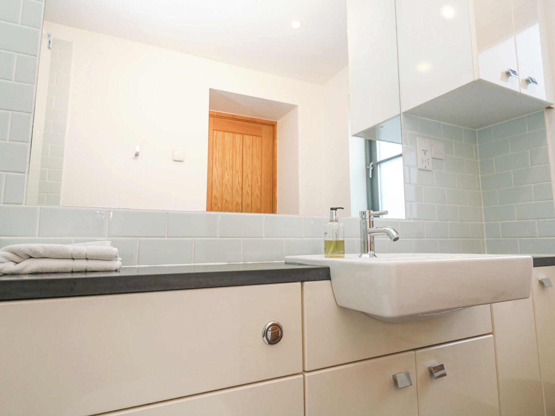 A modern bathroom with a white sink, a mirror, and a wooden door.