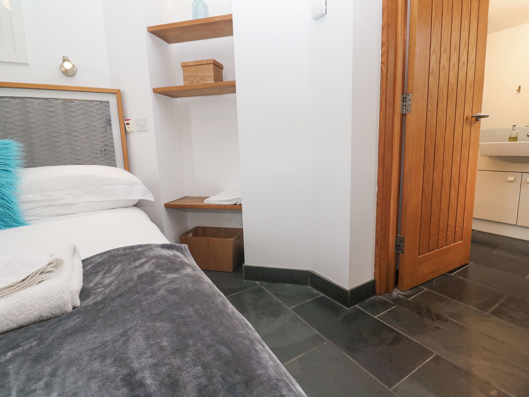 A bedroom with a bed, a bedside table, a nightstand, a wooden door, and a bathroom visible through an open door.