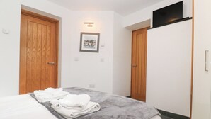 A hotel room with a bed, a grey blanket, and a folded white towel. There are wooden doors and a black TV mounted on the wall. - The Observatory Tower (Falmouth)