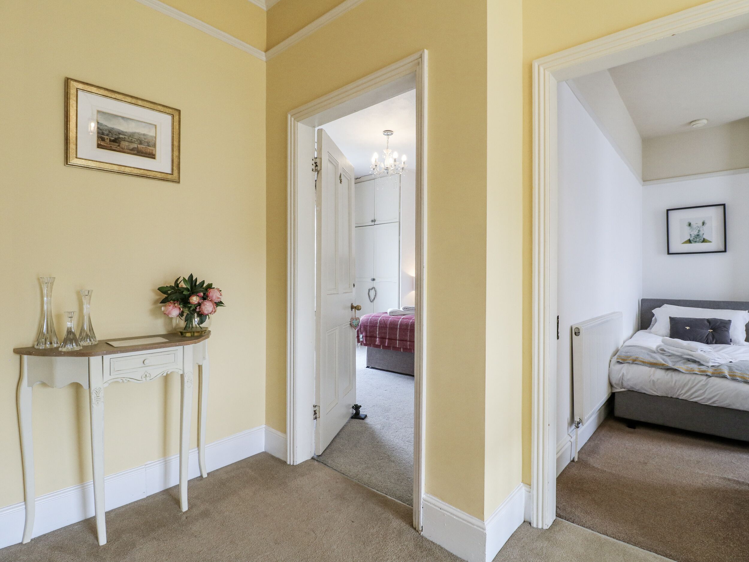 A bedroom with a bed, bedside table, and a nightstand. There is a door leading to another room.