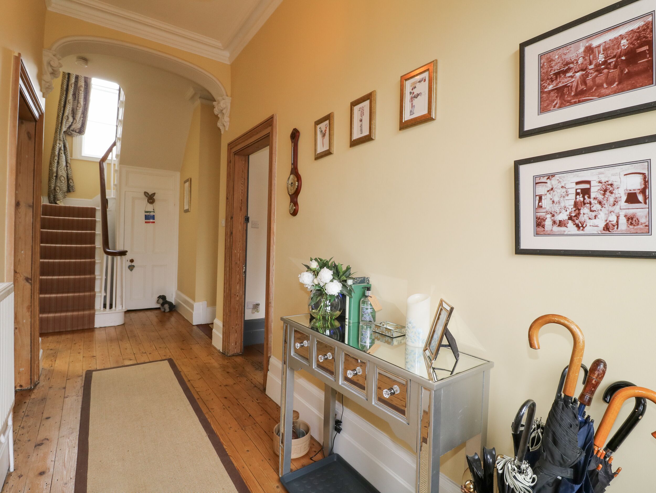 A hallway with a wooden staircase, a console table with decorative items, and framed pictures on the wall.