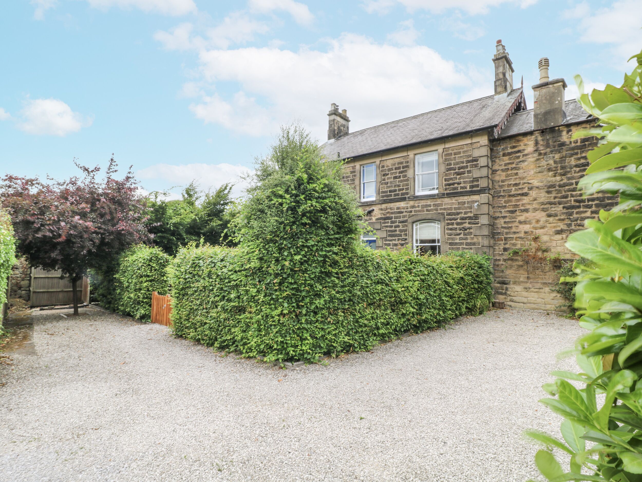 A stone house with a gravel driveway and a well-maintained hedge.
