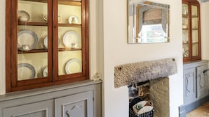 Een kamer met houten kastjes vol porselein, een open haard en een spiegel aan de muur.