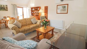 A living room with a sofa, a coffee table with flowers, a dining area with chairs and a table, and a radiator. - Millstone Cottages - Granary Cottage (Shrewsbury)