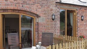 A brick building with a wooden fence, a table with chairs, and a window with a wooden frame. - Millstone Cottages - Granary Cottage (Shrewsbury)