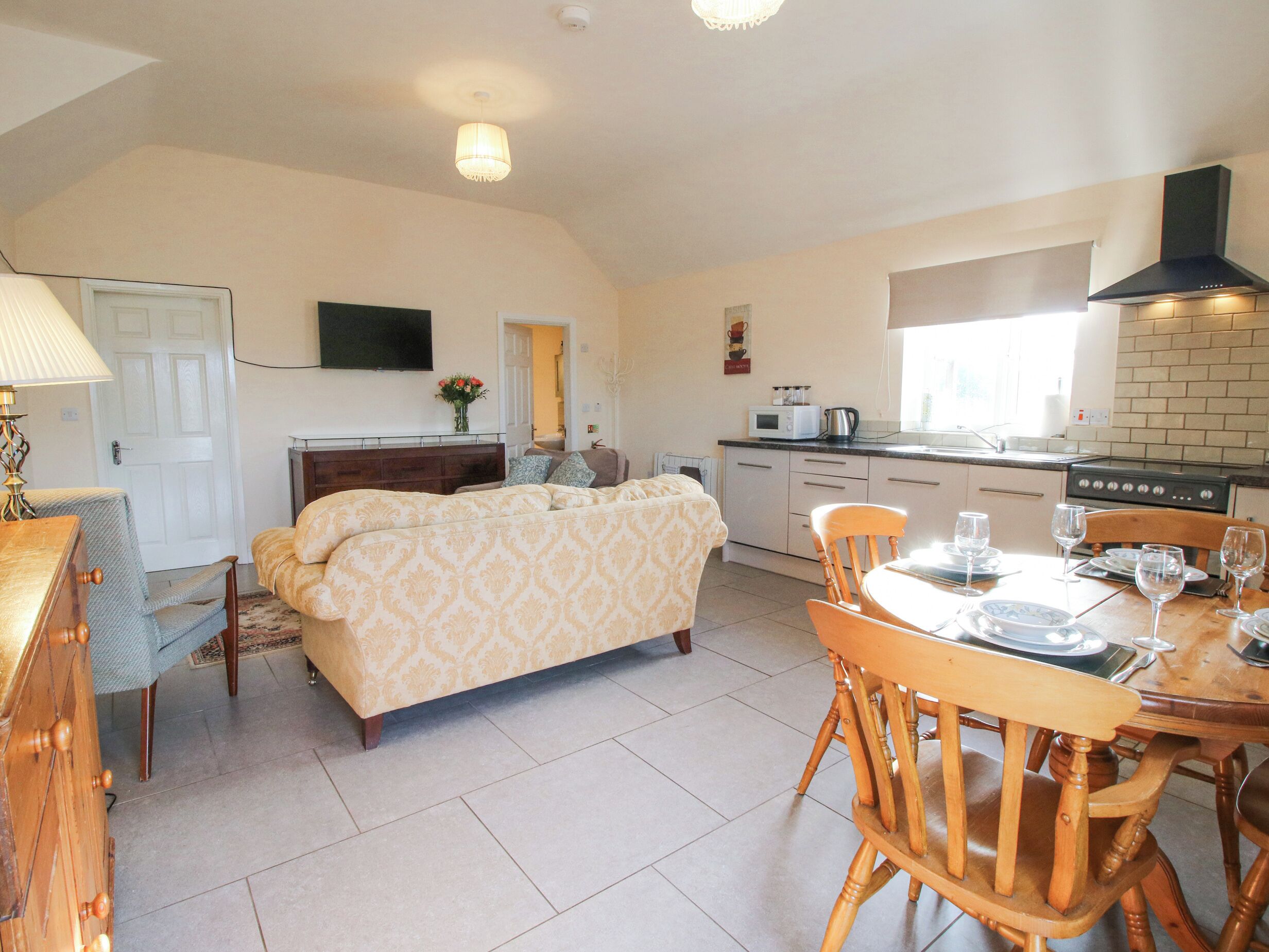 A compact living space with a bed, a dining table with chairs, a kitchenette, and a television mounted on the wall.