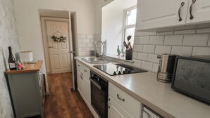 A compact kitchen with white cabinets, a wooden countertop, a built-in dishwasher, and a small refrigerator. - Camwy (Llanfairpwllgwyngyll)