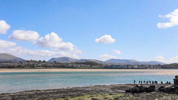 A coastal landscape with a clear sky, calm water, and distant mountains. - Camwy (Llanfairpwllgwyngyll)