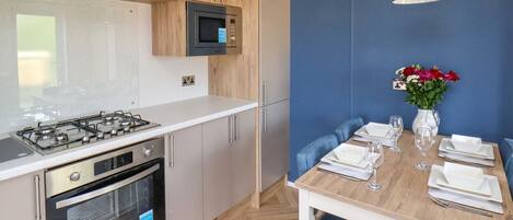 A modern kitchen with a gas stove, oven, microwave, and wooden cabinets. There is a dining table set with plates, glasses, and a vase of flowers.
