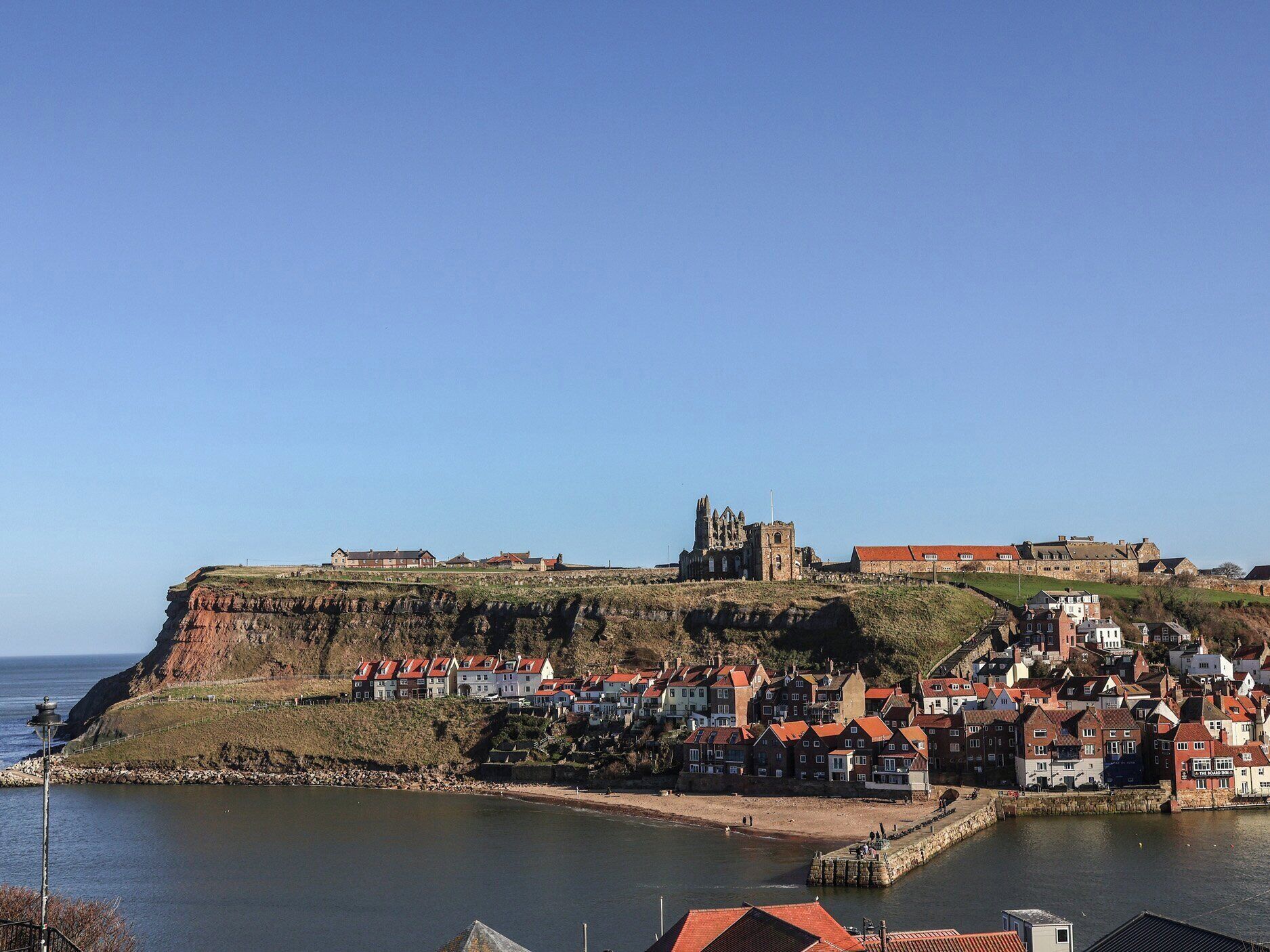 A coastal town with a prominent castle on a cliff, houses with red roofs, and a calm sea.