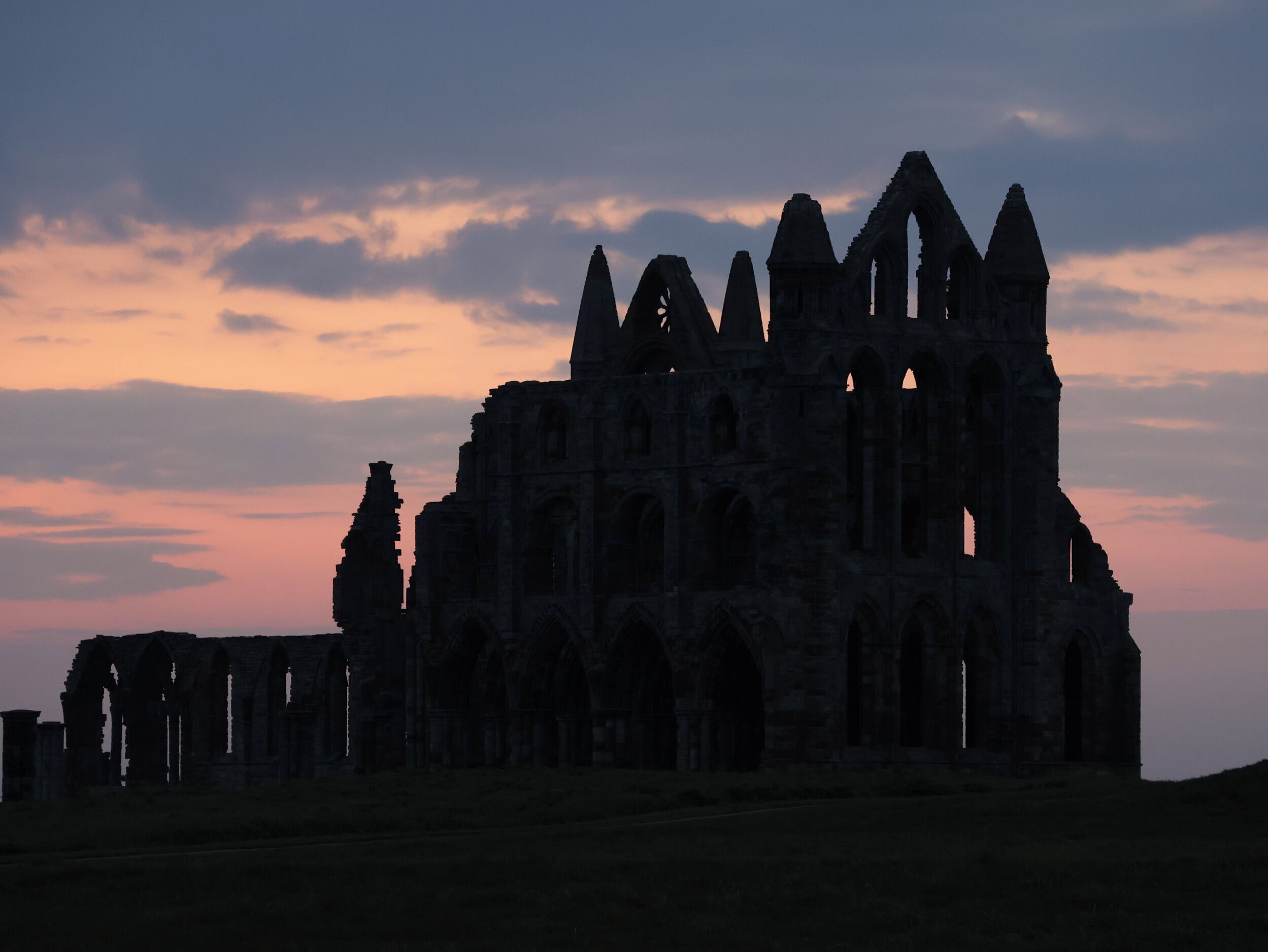 A large, historic stone structure with multiple arches and towers, likely a cathedral or abbey, set against a twilight sky.