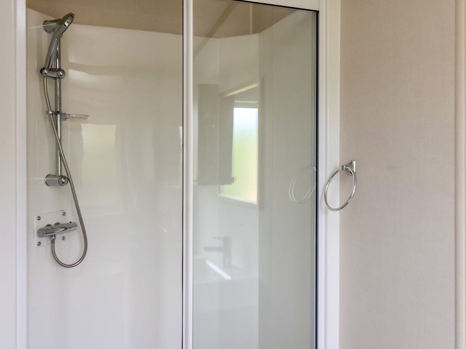 A glass-enclosed shower with a handheld showerhead and a handheld faucet.