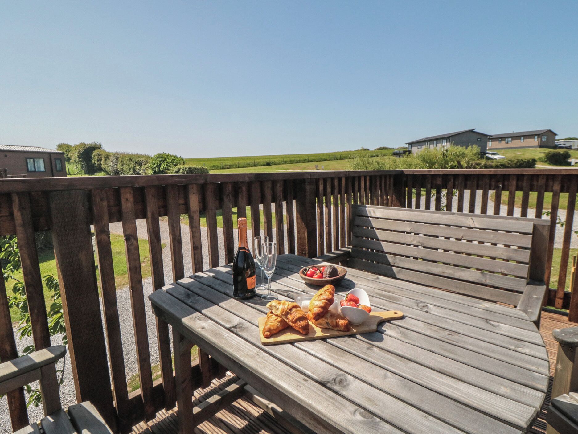 Une terrasse en bois avec une table dressée pour un repas, comprenant des croissants, des fraises et une bouteille de champagne.