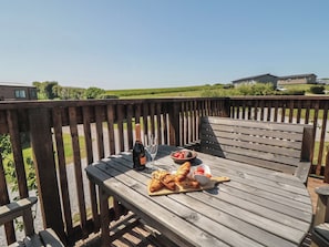 A wooden deck with a table set for a meal, including croissants, strawberries, and a bottle of champagne.