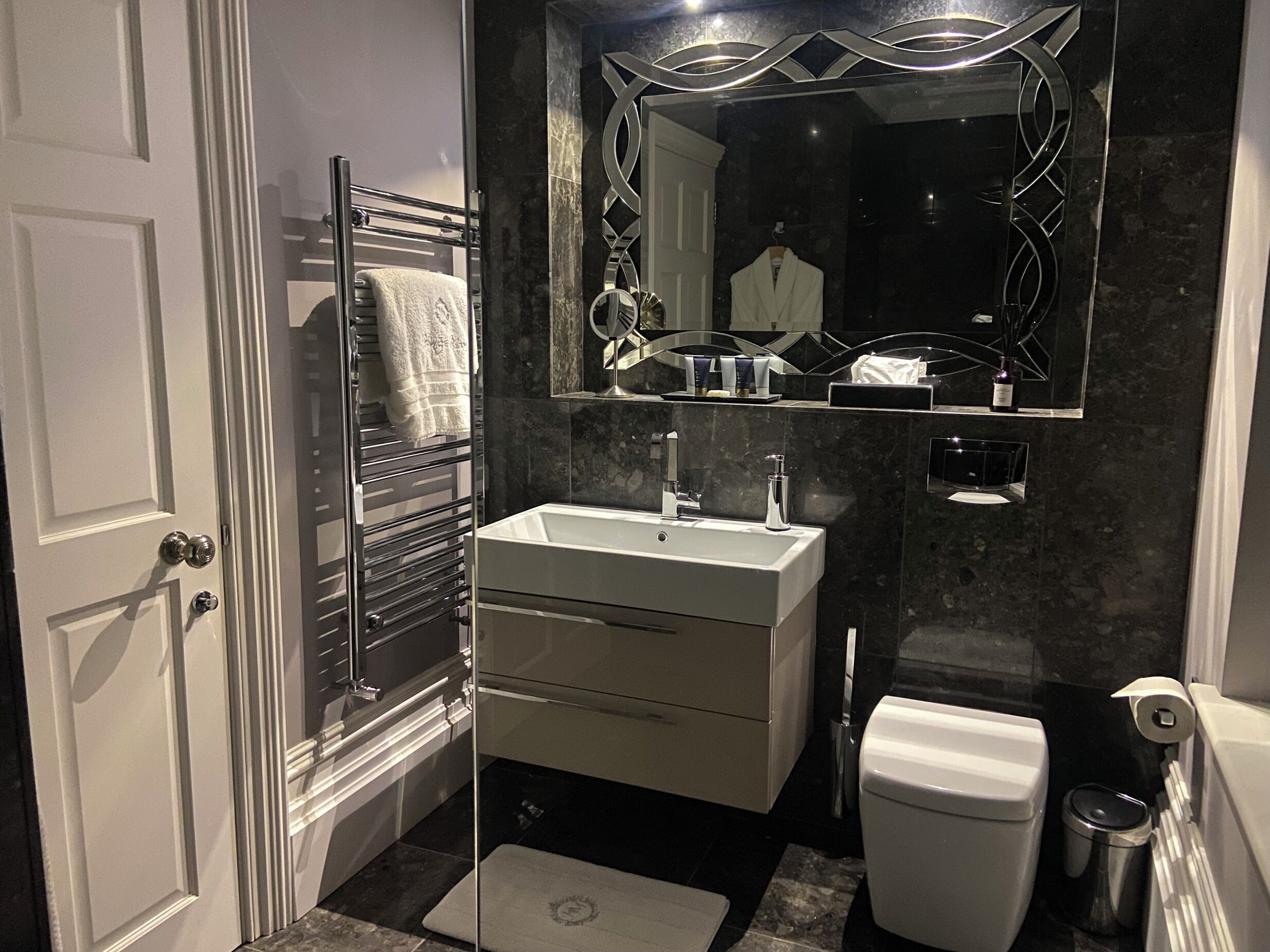 Une salle de bain moderne avec un lavabo blanc, un miroir, un porte-serviettes et des toilettes.