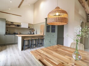 A modern kitchen with a wooden island, bar stools, and a hanging light fixture. - Hazel Cottage - Fold Yards (Matlock)