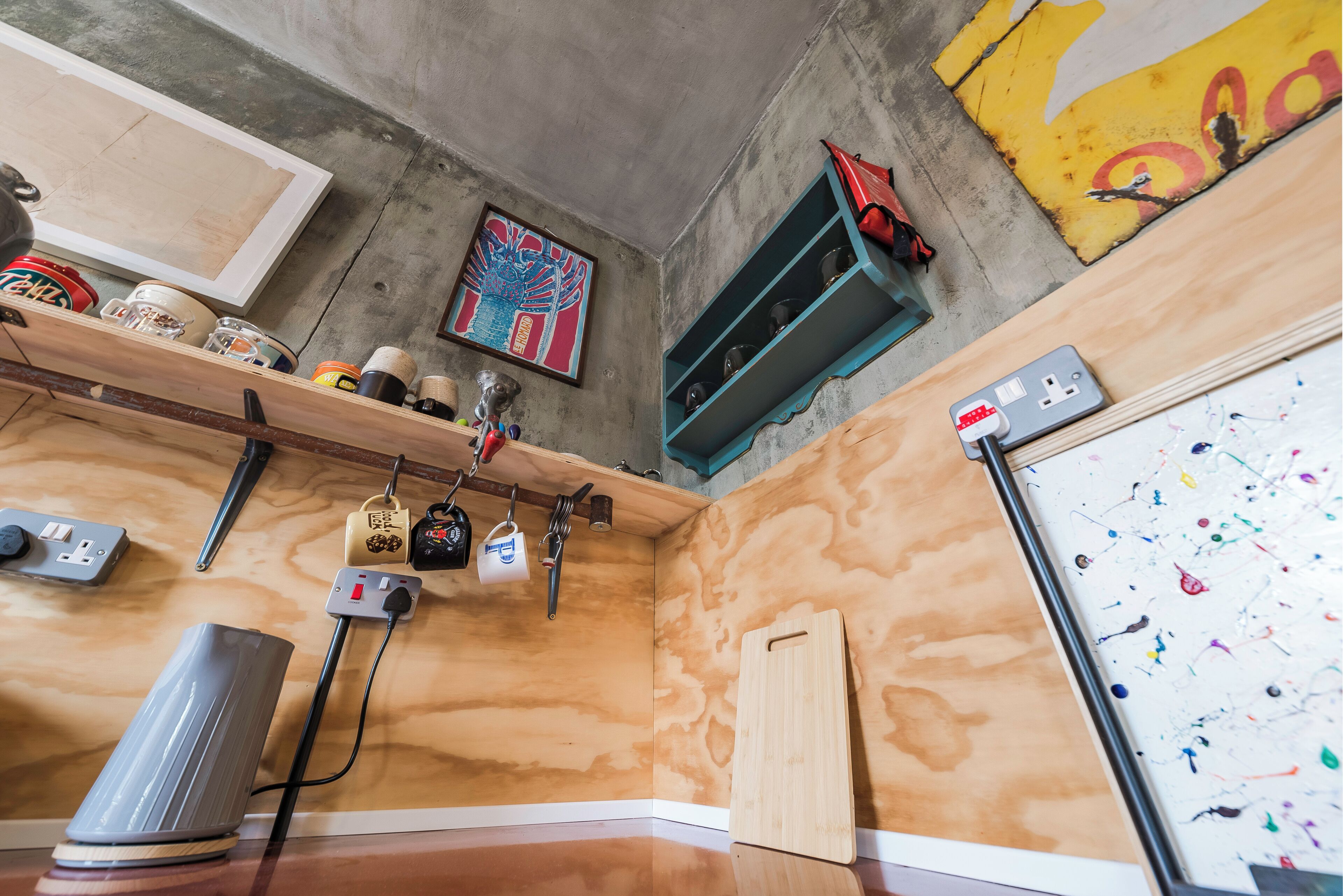 Una cocina con encimera de madera, una cafetera, un estante con utensilios de cocina, un cuadro en la pared y una ventana con vistas al exterior.