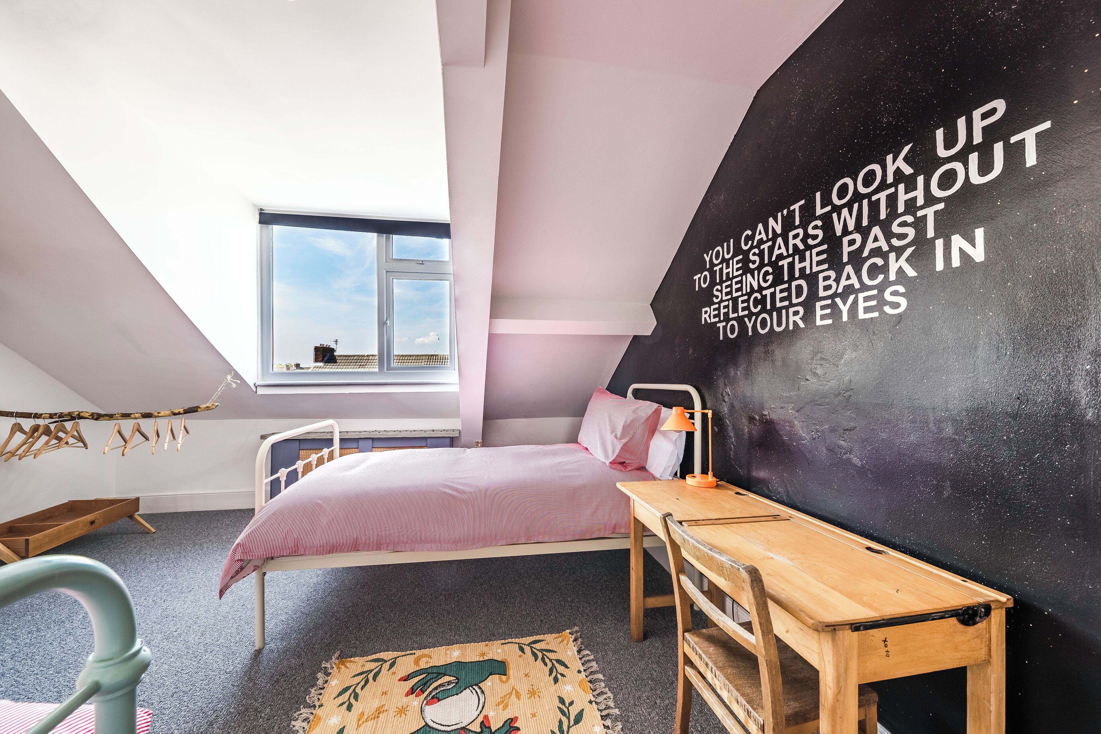 A bedroom with a bed, a desk, and a wall with motivational text.