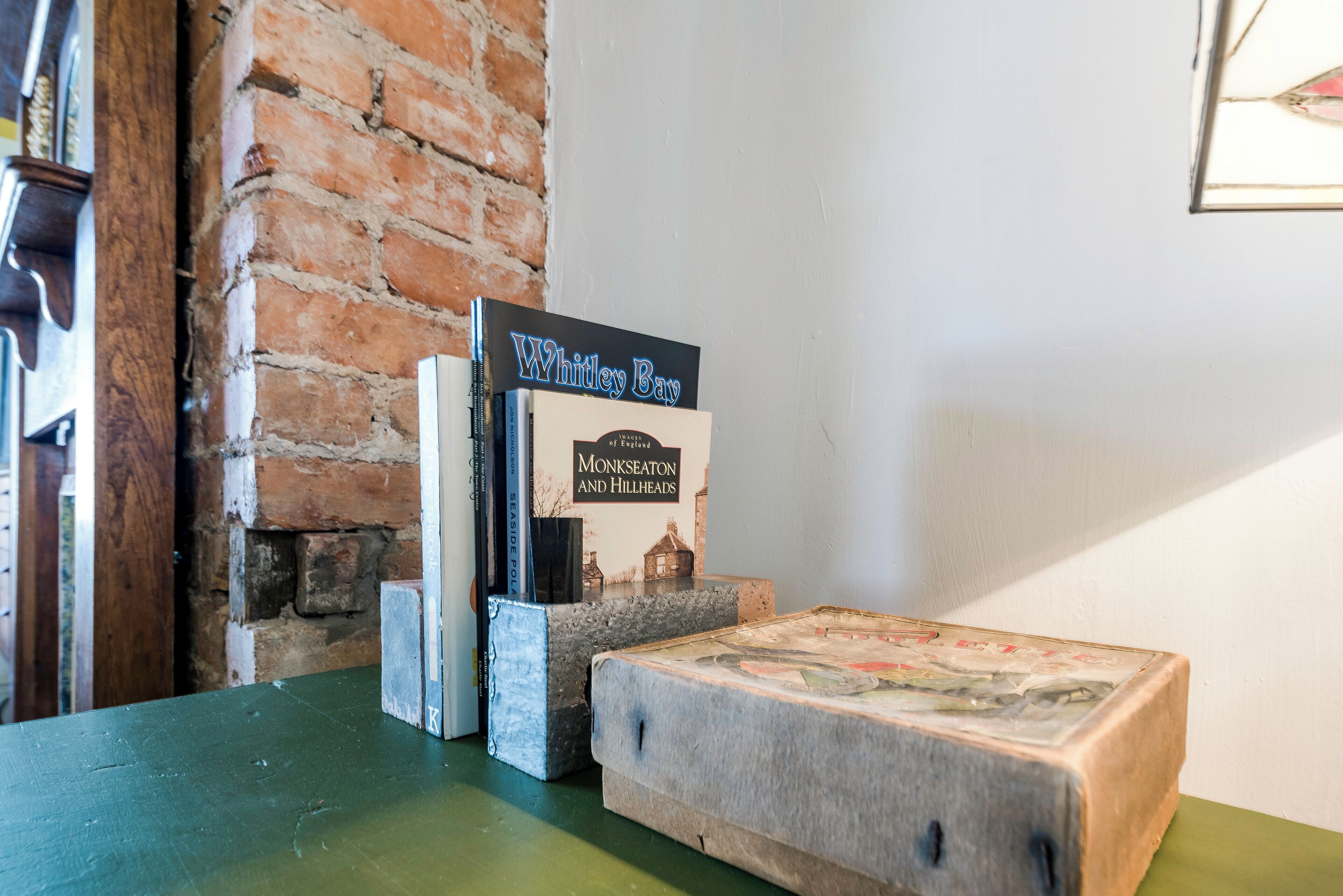 Una estantería con libros y un cuadro enmarcado, una pared de ladrillo y una mesa verde.