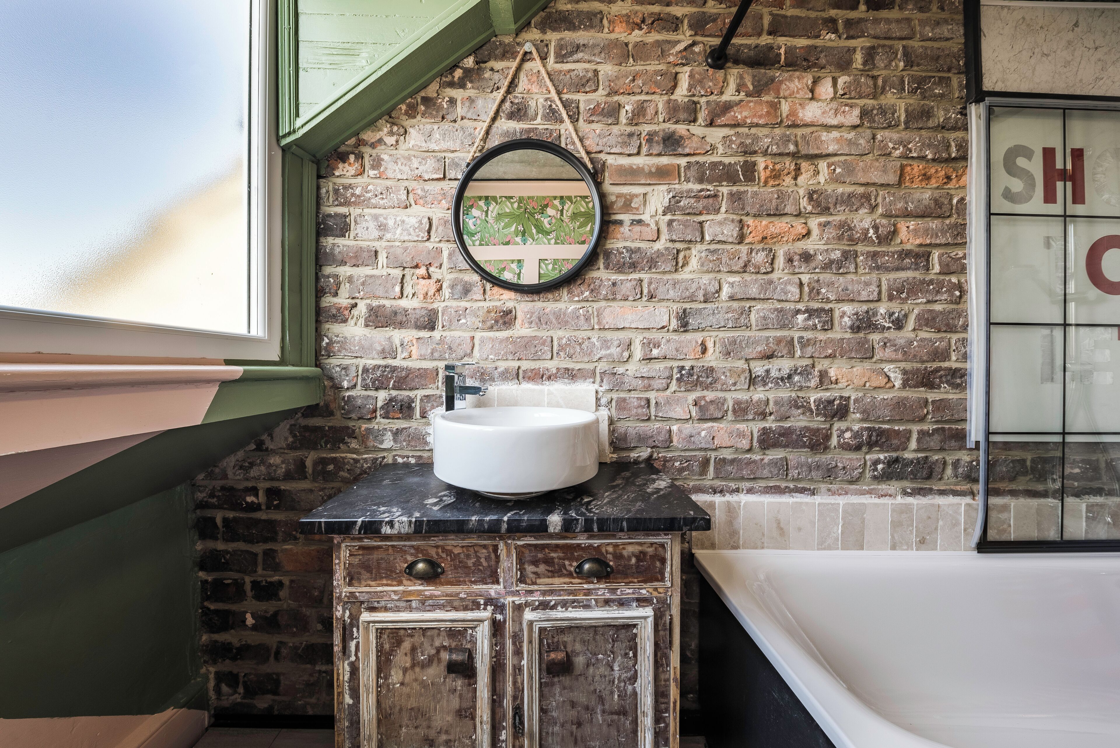 Une salle de bain avec un mur en briques, un miroir rond, un lavabo et une baignoire.