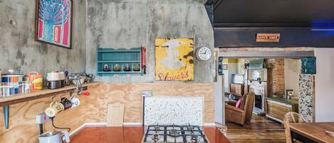 A kitchen with a gas stove, wooden cabinets, and a coffee machine. There is a clock on the wall and a sign that says "Dance More".