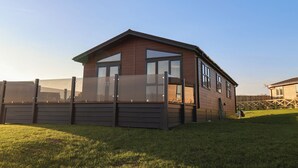 Une maison moderne avec une façade en bois, de grandes fenêtres et une cour clôturée.